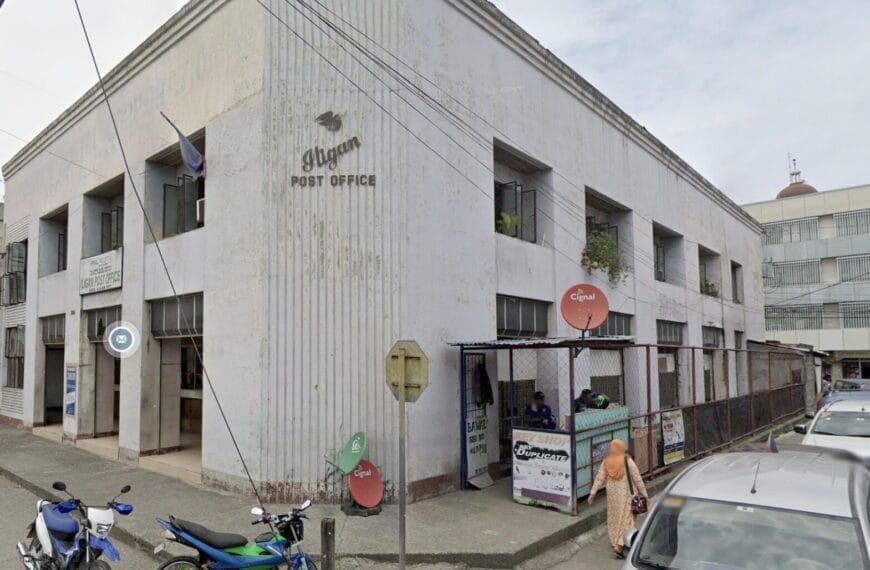 baguios post office building, philippines, with motorcycles and cars parked outside on a cloudy day.